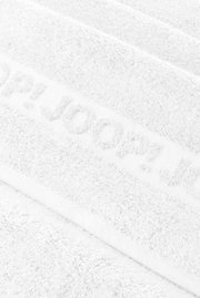 Close-up vanuit een schuin bovenaanzicht van een witte, zachte handdoek met het ingeweven opschrift „HUGO“.