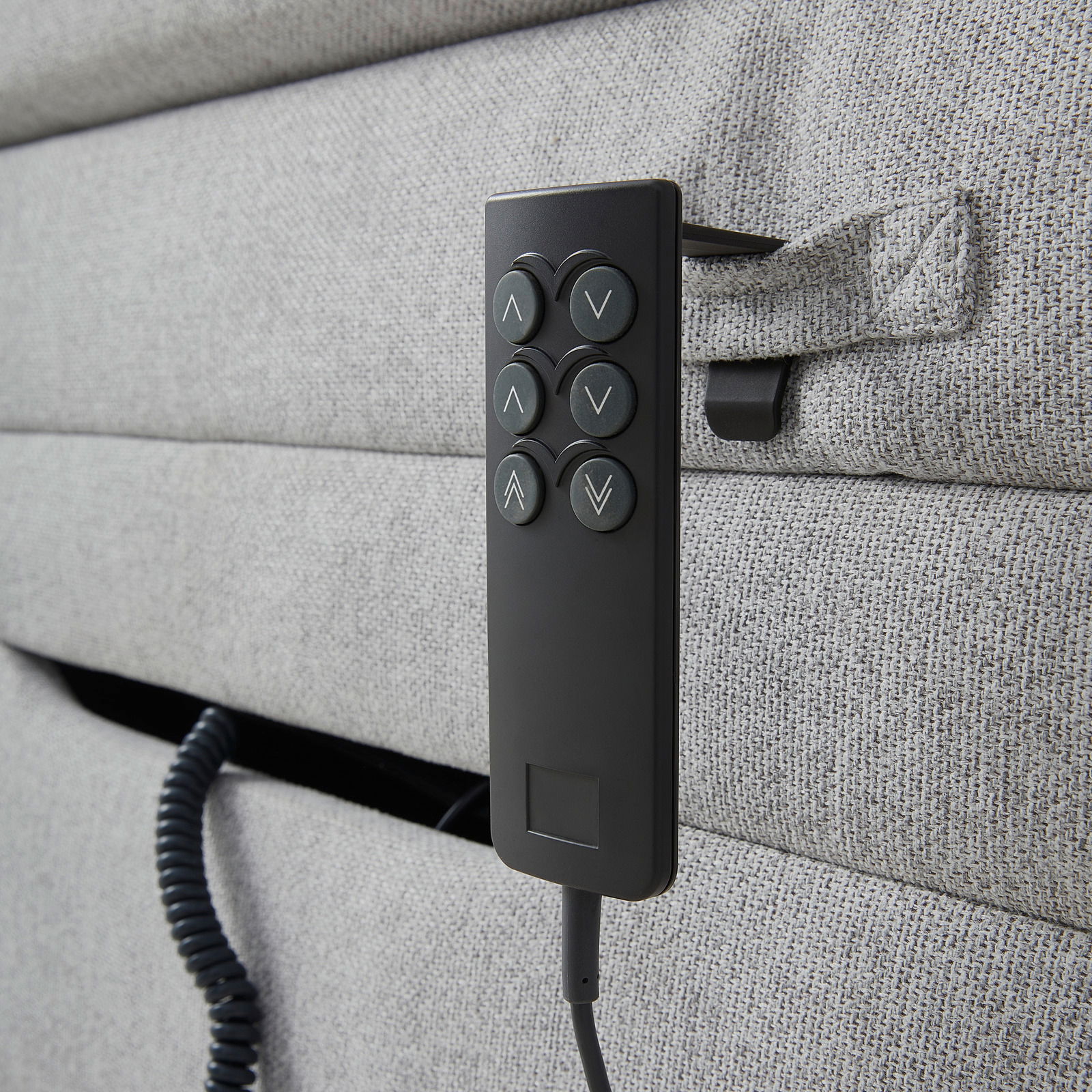 Nahaufnahme eines grauen Boxspringbetts mit einer schwarzen Fernbedienung an der Seite, seitliche Perspektive