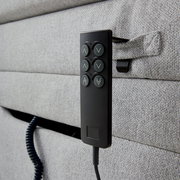 Nahaufnahme eines grauen Boxspringbetts mit einer schwarzen Fernbedienung an der Seite, seitliche Perspektive