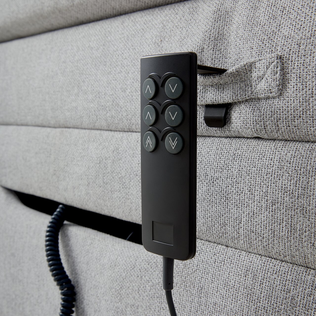 Nahaufnahme eines grauen Boxspringbetts mit einer schwarzen Fernbedienung an der Seite, seitliche Perspektive