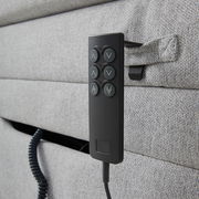 Nahaufnahme eines grauen Boxspringbetts mit einer schwarzen Fernbedienung an der Seite, seitliche Perspektive