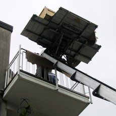 Ein Sofa, das mit Hilfe eines Flaschenzuges aus dem Fenster gehievt wird, bei klarem Himmel.