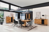 Moderne Esszimmermöbel in einem hellen Raum mit großen Fenstern, bestehend aus einem Holztisch, grauen Stühlen und einem Sideboard, aus der Perspektive des Raumes betrachtet.