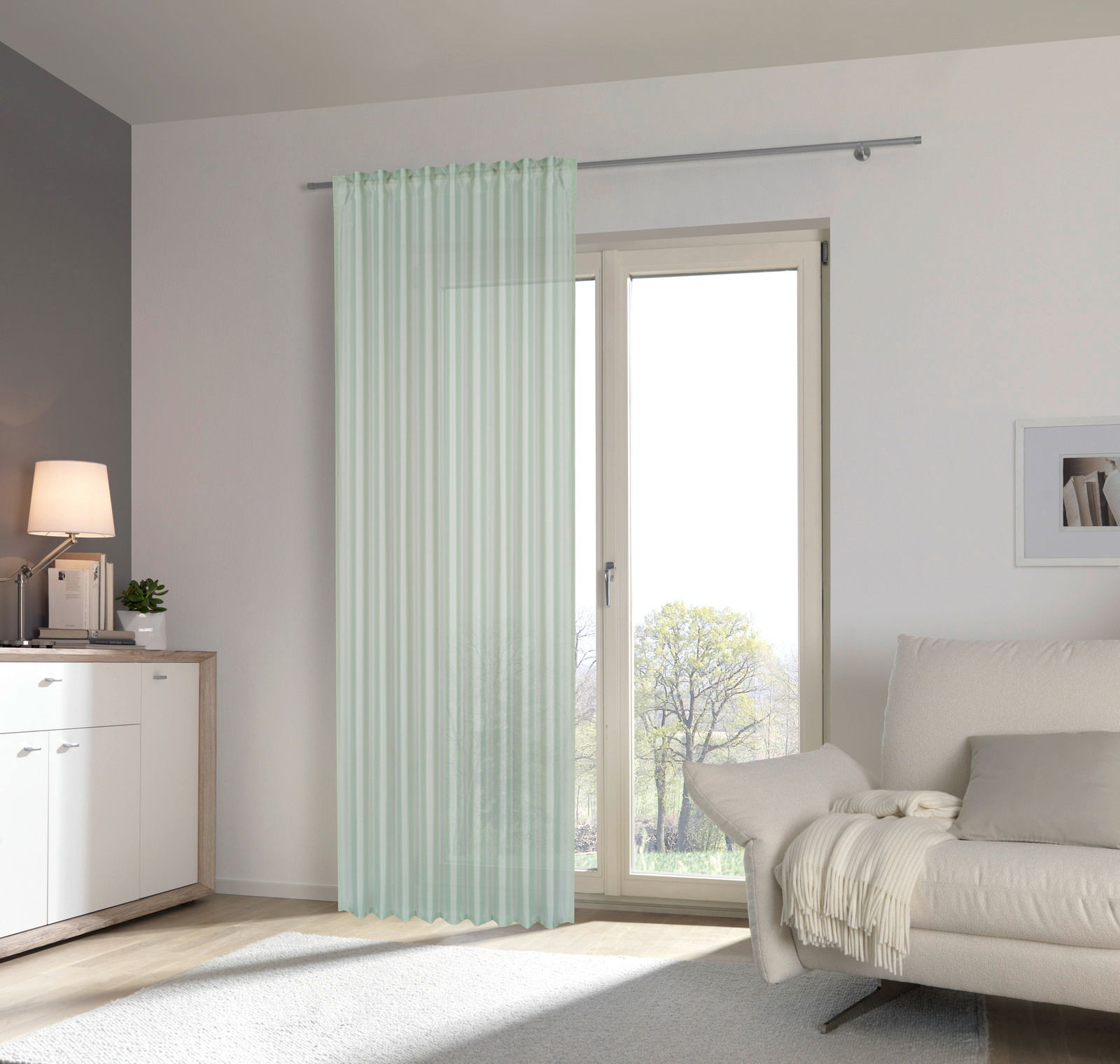 Moderner, transparenter Fertigvorhang in hellem Mintgrün, aufgehängt vor einer großen Fensterfront in einem stilvoll eingerichteten Wohnzimmer. Perspektive von vorne.