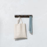 Wandgarderobe aus dunklem Holz mit mehreren Haken, an denen eine beige Stofftasche und ein blaues Handtuch hängen, frontal betrachtet.