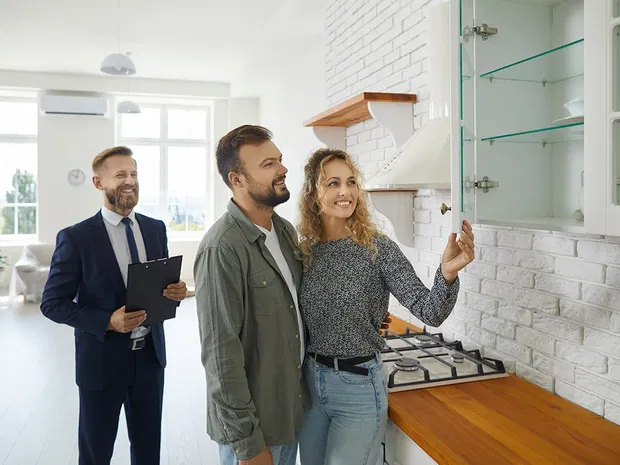 Ein glückliches Paar schaut sich mit einem Küchenberater eine helle Küche an