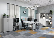 Moderne Büroumgebung mit Schreibtischen, Rollcontainer und Aktenschränken in einem hellen Raum mit großen Fenstern, seitliche Perspektive.