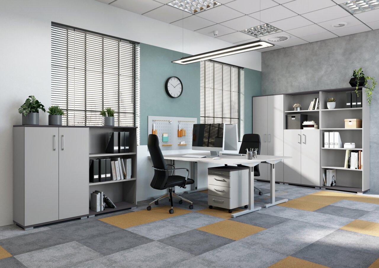 Moderne Büroumgebung mit Schreibtischen, Rollcontainer und Aktenschränken in einem hellen Raum mit großen Fenstern, seitliche Perspektive.