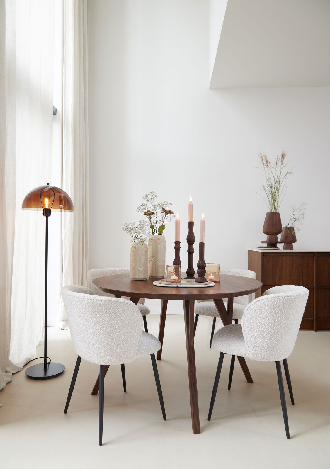 Runder Esstisch QUENZA aus Holz mit dekorativen Kerzen und Vasen, umgeben von vier gepolsterten Stühlen in einem hellen, modernen Raum. Seitliche Perspektive.