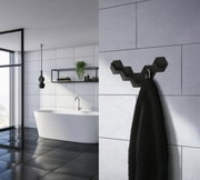 Schwarzer, mattierter Edelstahlhaken in sechseckigem Design, an einer Badezimmerwand montiert, mit einem Handtuch daran hängend. Perspektive von der Seite.