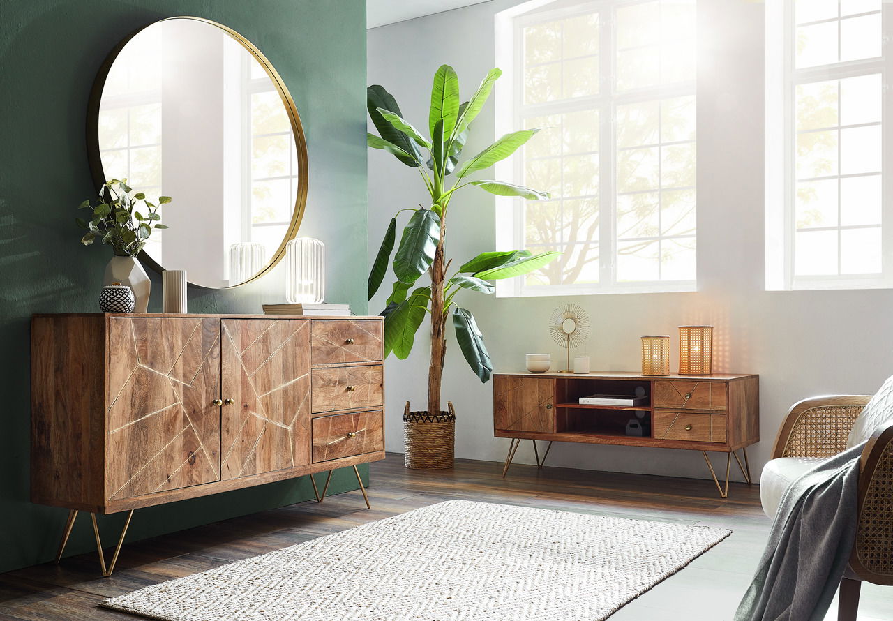 TV-Lowboard aus Holz mit geometrischem Design, goldenen Griffen und schrägen Beinen, in einem modernen Wohnzimmer mit großem Fenster und Pflanzen, seitliche Perspektive.