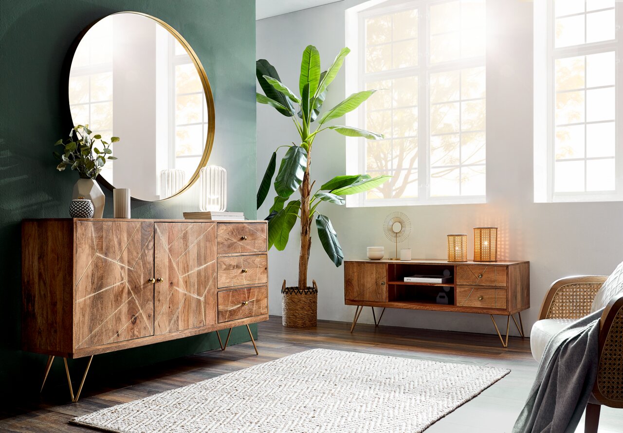 TV-Lowboard aus Holz mit geometrischem Design, goldenen Griffen und schrägen Beinen, in einem modernen Wohnzimmer mit großem Fenster und Pflanzen, seitliche Perspektive.