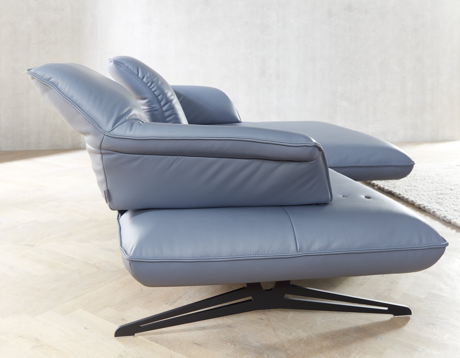 Seitliche Ansicht einer modernen Longchairkombination in blauem Leder mit schwarzem Metallfuß auf hellem Holzboden.