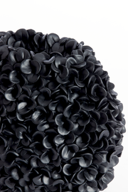 Nahaufnahme einer dekorativen Vase mit schwarzer, blütenartiger Struktur, seitliche Perspektive.