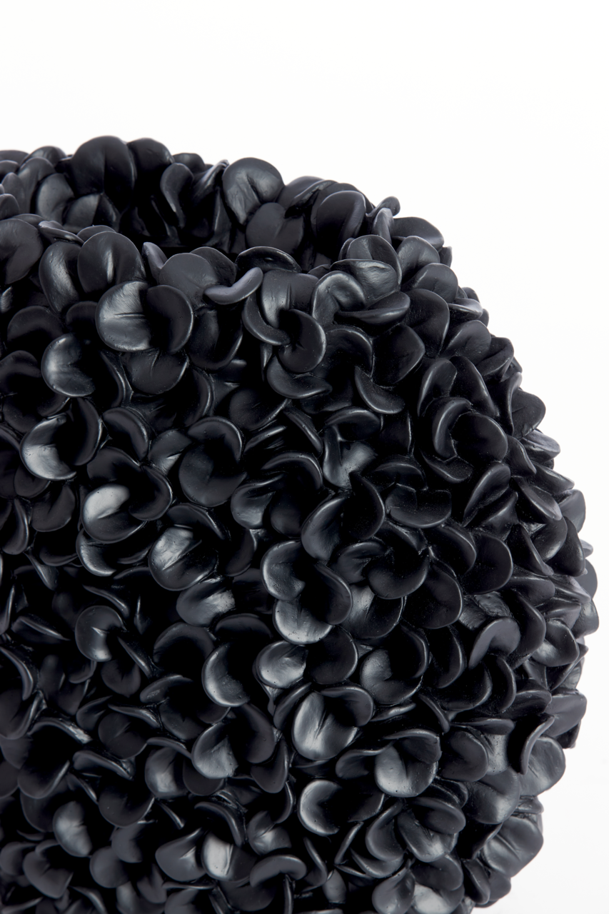 Nahaufnahme einer dekorativen Vase mit schwarzer, blütenartiger Struktur, seitliche Perspektive.