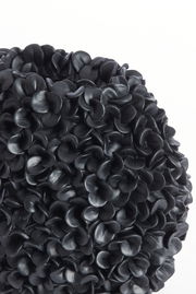 Nahaufnahme einer dekorativen Vase mit schwarzer, blütenartiger Struktur, seitliche Perspektive.