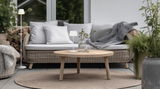 Moderne Akku-Stehleuchte SUAREZ in einem gemütlichen Wohnzimmer mit Rattanmöbeln und Pflanzen, seitliche Perspektive.