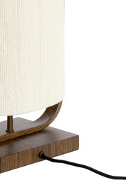 Detailaanzicht van opzij van een tafellamp met crèmekleurige stoffen kap, gebogen houten frame, rechthoekige houtlook voet en zwart snoer