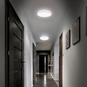 Twee ronde, opbouw LED-plafondlampen die een moderne gang verlichten, gefotografeerd in perspectief van onderaf richting het einde van de hal.