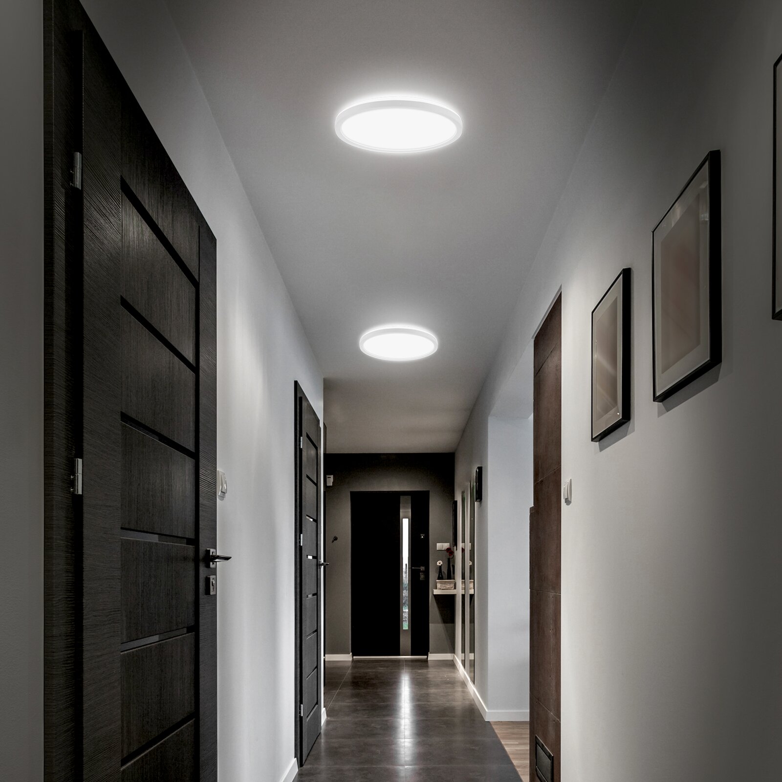 Twee ronde, opbouw LED-plafondlampen die een moderne gang verlichten, gefotografeerd in perspectief van onderaf richting het einde van de hal.