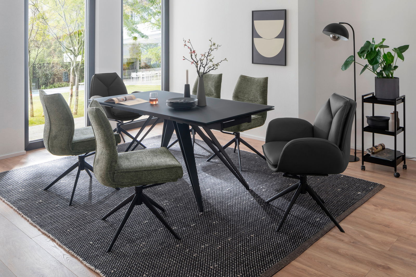 Zurbrüggen Armlehnstuhl ASSENTO Esszimmer mit modernem Tisch und Stühlen in einem hellen Raum mit großen Fenstern, seitliche Perspektive.