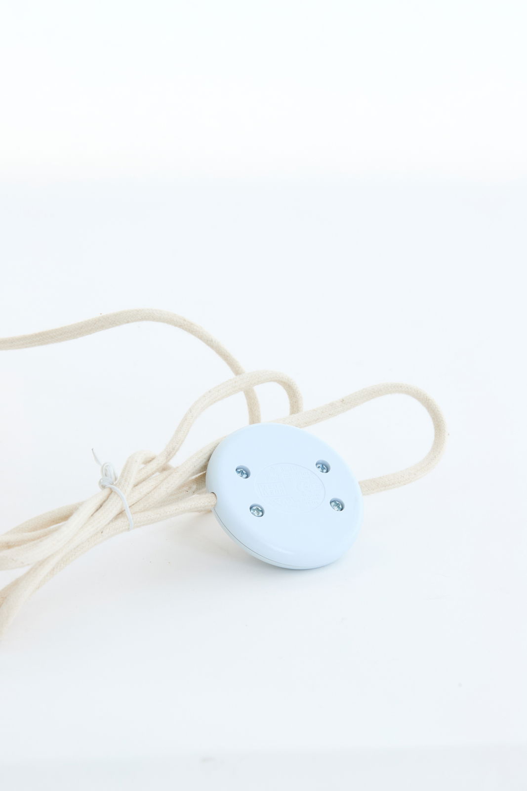 Nahaufnahme eines weißen Kabels mit einem runden, blauen Schalter, Teil einer Stehleuchte.