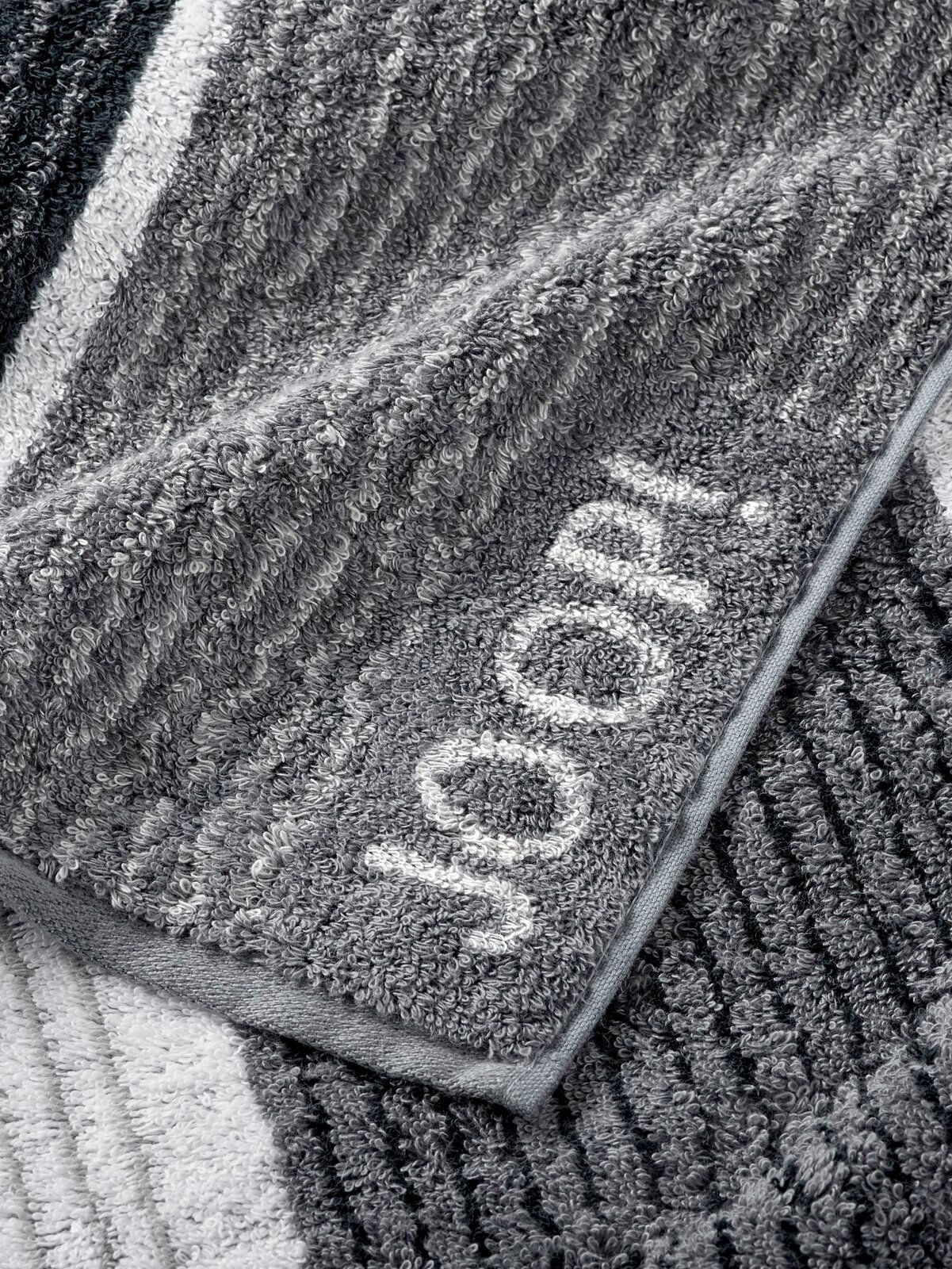 Graues Handtuch mit eingewebtem Schriftzug 'JOOP!' in Nahaufnahme, zeigt die weiche Textur und das Streifenmuster.