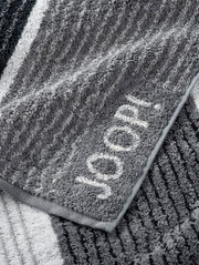 Graues Handtuch mit eingewebtem Schriftzug 'JOOP!' in Nahaufnahme, zeigt die weiche Textur und das Streifenmuster.