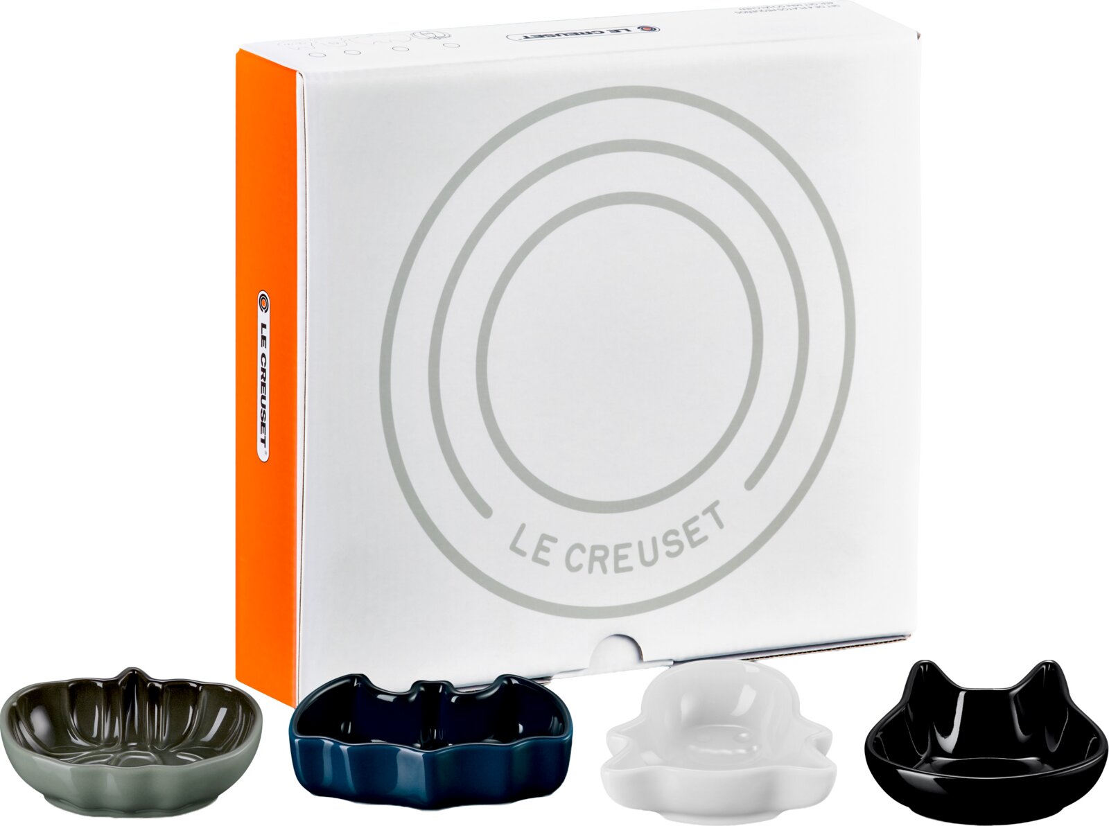 Vier dekorative Le Creuset Keramikschälchen in Grau, Blau, Weiß und Schwarz vor der Originalverpackung, aus leicht erhöhter Frontalperspektive