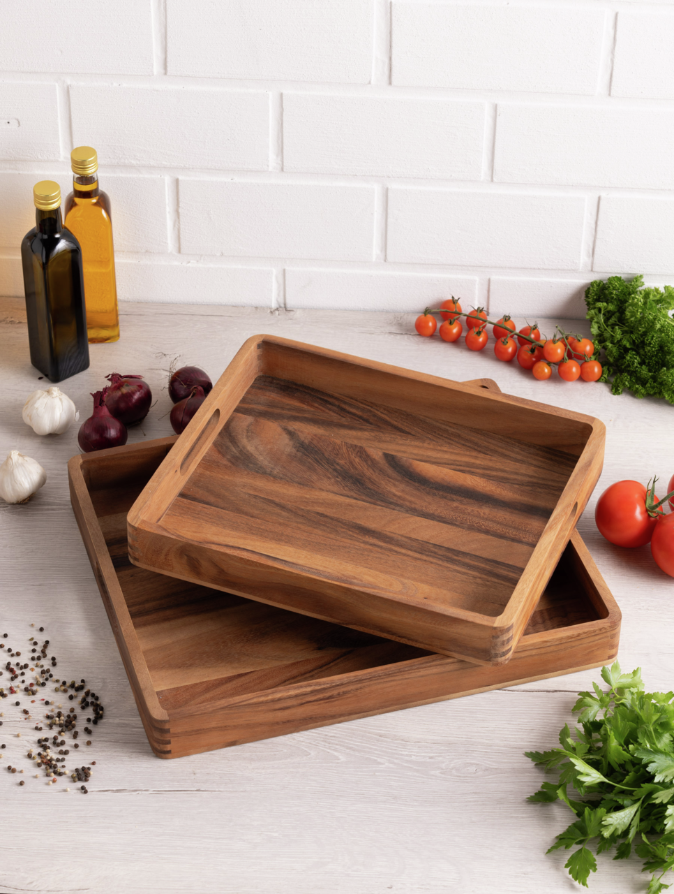 Zwei hölzerne Tabletts in rechteckiger Form, übereinander gestapelt, umgeben von frischen Zutaten wie Tomaten, Kräutern und Gewürzen, aus der Vogelperspektive fotografiert.