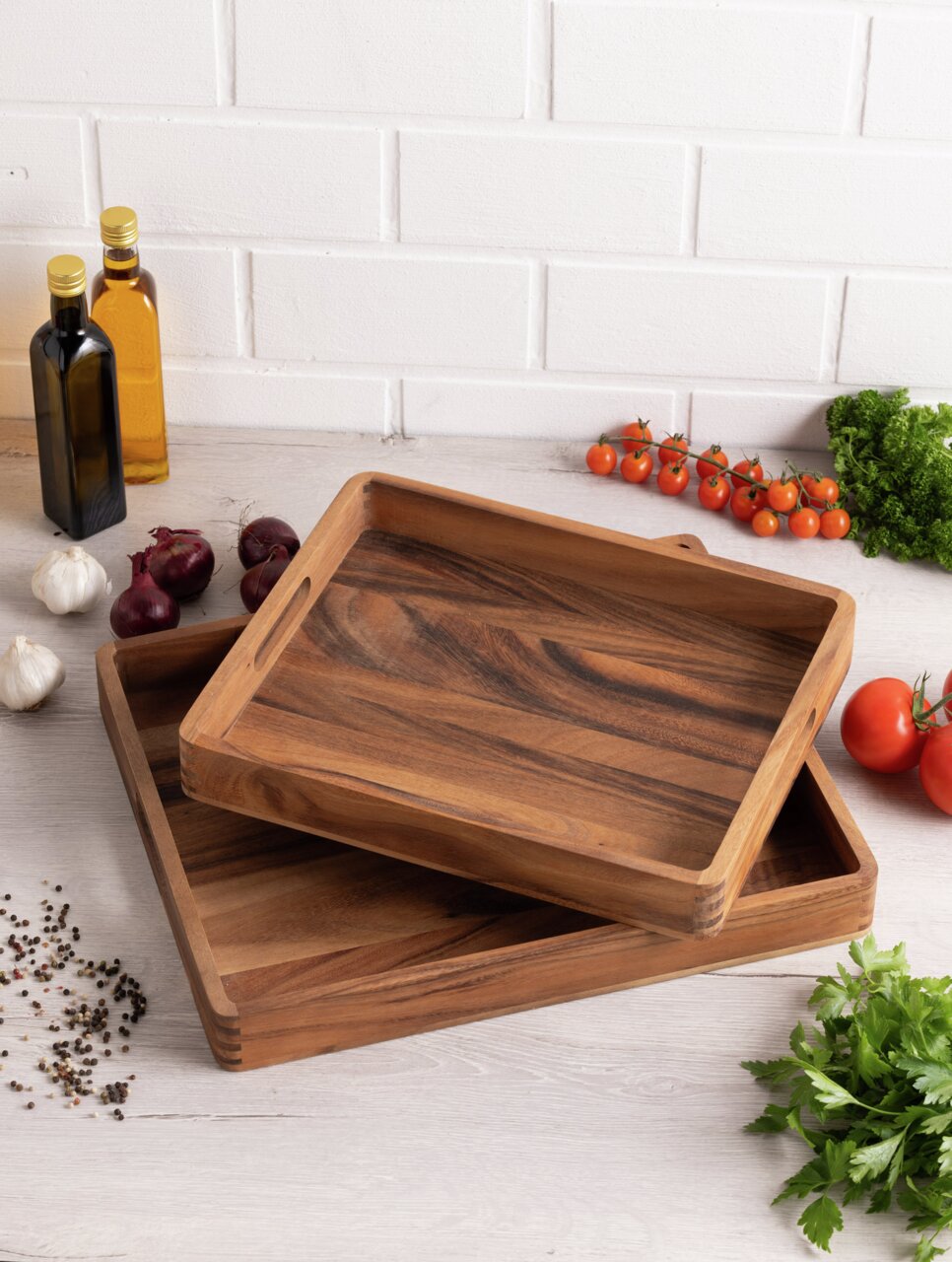 Twee rechthoekige houten dienbladen, op elkaar gestapeld en omringd door verse ingrediënten zoals tomaten, kruiden en specerijen, gefotografeerd vanuit vogelperspectief.