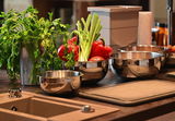 Frische Paprika, Frühlingszwiebeln und Petersilie in Edelstahl-Schüsseln auf moderner Küchenarbeitsfläche.