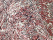 Nahaufnahme eines Designer-Teppichs mit gemusterten Farben in Rot-, Grau- und Beigetönen, aus seitlicher Perspektive aufgenommen.