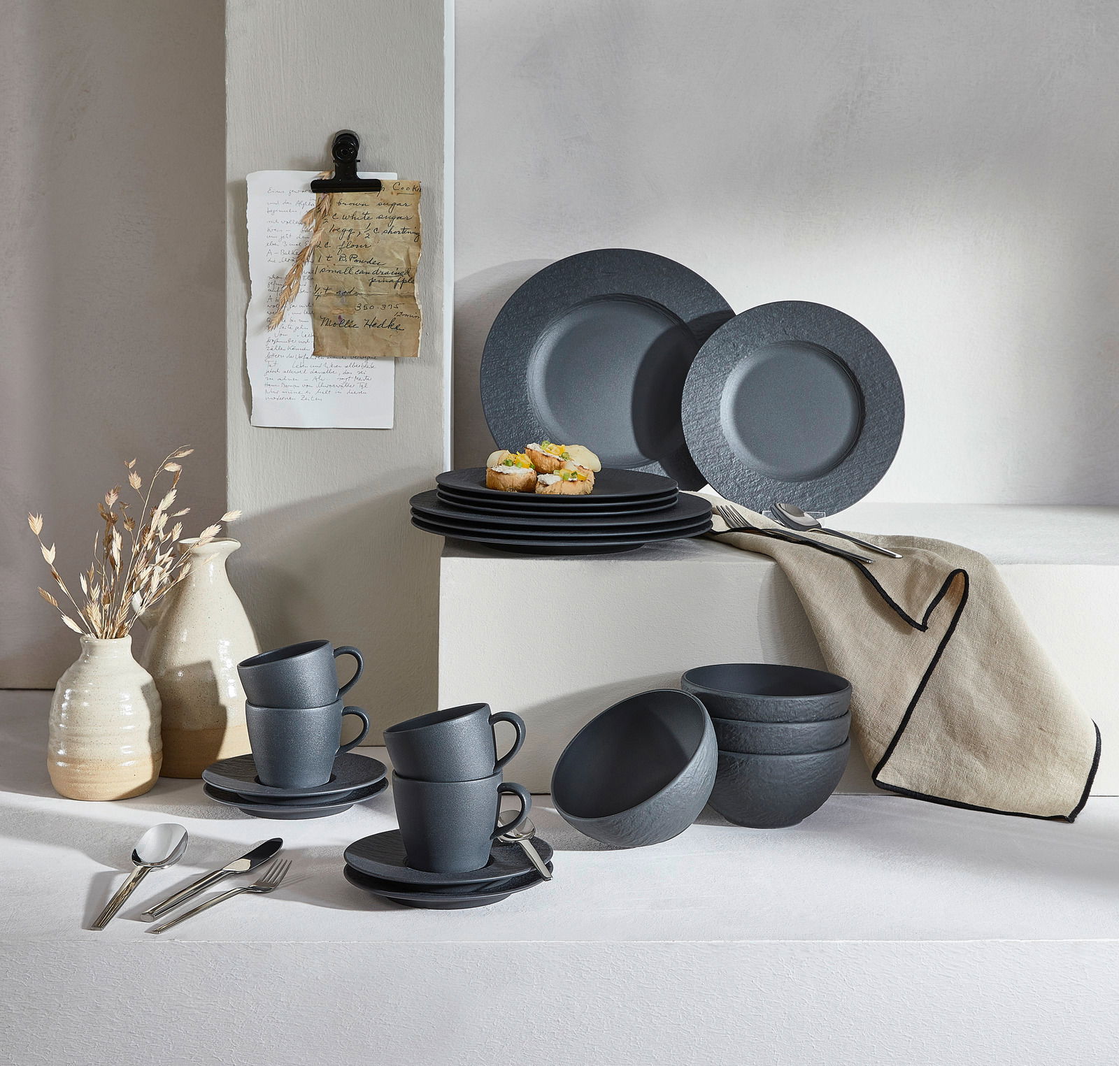 Elegantes 20-teiliges Geschirrset in dunklem Steingrau, bestehend aus Tellern, Tassen und Schalen, stilvoll arrangiert auf einem Tisch mit seitlicher Perspektive.