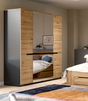 Großer Kleiderschrank in Holzoptik mit grauen Seiten und mittigen Spiegeltüren, im Schlafzimmer aus frontaler Perspektive leicht schräg von links fotografiert.