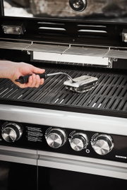 Hand hält eine BBQ Reinigungsbürste SlideX über einem Grillrost, seitliche Perspektive