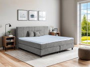 Graues Boxspringbett in modernem Schlafzimmer, seitliche Perspektive mit Tageslicht durch großes Fenster