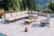 Moderne Loungegarnitur mit hellem Polster und Holzdetails auf einer Terrasse mit Blick auf bewaldete Berge, seitliche Perspektive.