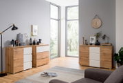 Moderne houten ladekast met witte ladefronten, gefotografeerd vanuit een zijdelingse hoek in een lichte ruimte met grote ramen.