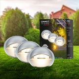 Erweiterungsset aus Edelstahl mit runden, leuchtenden Lampen, präsentiert auf einer grünen Wiese mit Verpackung im Hintergrund. Perspektive: Frontalansicht.