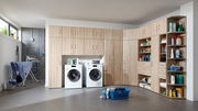 Eckschrank-Aufsatz in einer Waschküche mit Holzoptik, umgeben von Waschmaschinen und Regalen, perspektivisch von vorne rechts.