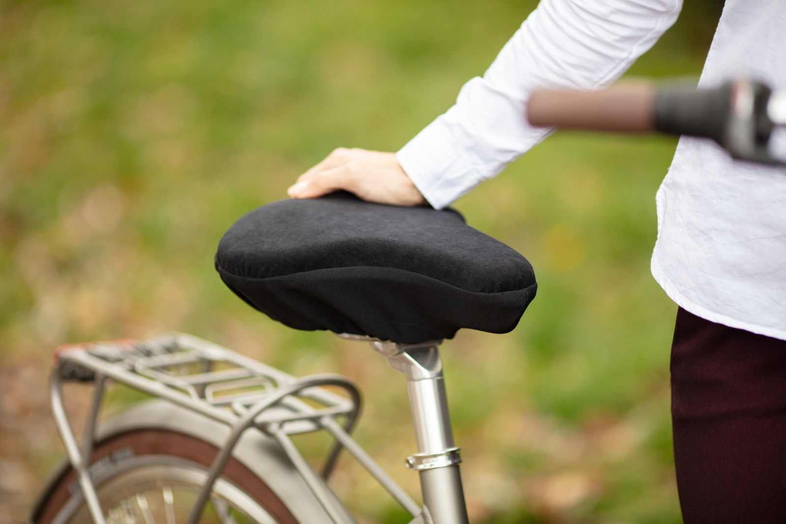 Tempur Fahrradsattelkissen S Nahaufnahme eines schwarzen Tempur Fahrradsattelkissens auf einem Fahrrad, mit einer Hand, die es von oben berührt.