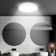 Moderne LED-Deckenleuchte mit Bewegungssensor, von unten betrachtet, in einem stilvollen Badezimmer mit zwei runden Spiegeln und weißen Fliesen.
