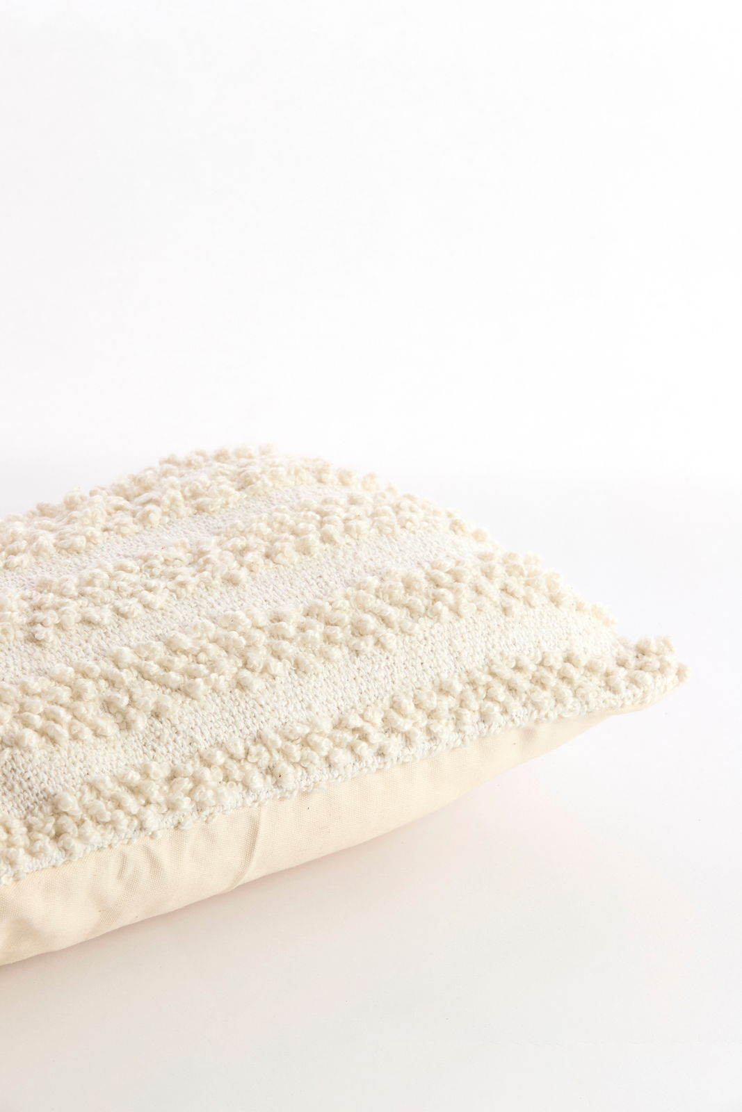 Nahaufnahme eines strukturierten, cremefarbenen Kissens mit dekorativem Muster, seitliche Perspektive