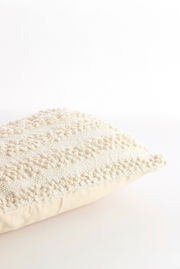 Nahaufnahme eines strukturierten, cremefarbenen Kissens mit dekorativem Muster, seitliche Perspektive