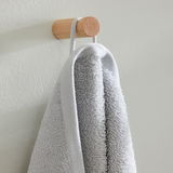 Graues Frottierhandtuch, das an einem runden Holzknauf an der Wand hängt, seitliche Perspektive.