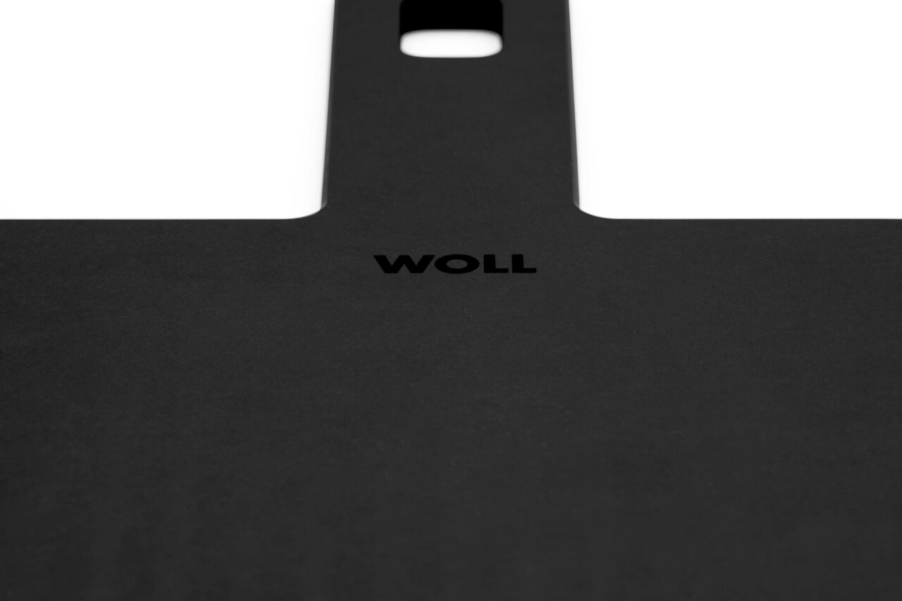 Nahaufnahme eines schwarzen Schneidebretts mit dem Logo 'WOLL' in der Mitte, perspektivisch von oben fotografiert.