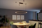 Moderne schwarze LED-Ring-Pendelleuchte mit warmweißem Licht über einem Esstisch in Wohnküche, Perspektive leicht von unten mit Blick nach oben auf die Deckenmontage