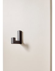 Schwarzer, rechtwinkliger Wandhaken aus Metall an heller Wand, seitliche Perspektive mit sichtbarem Schattenwurf