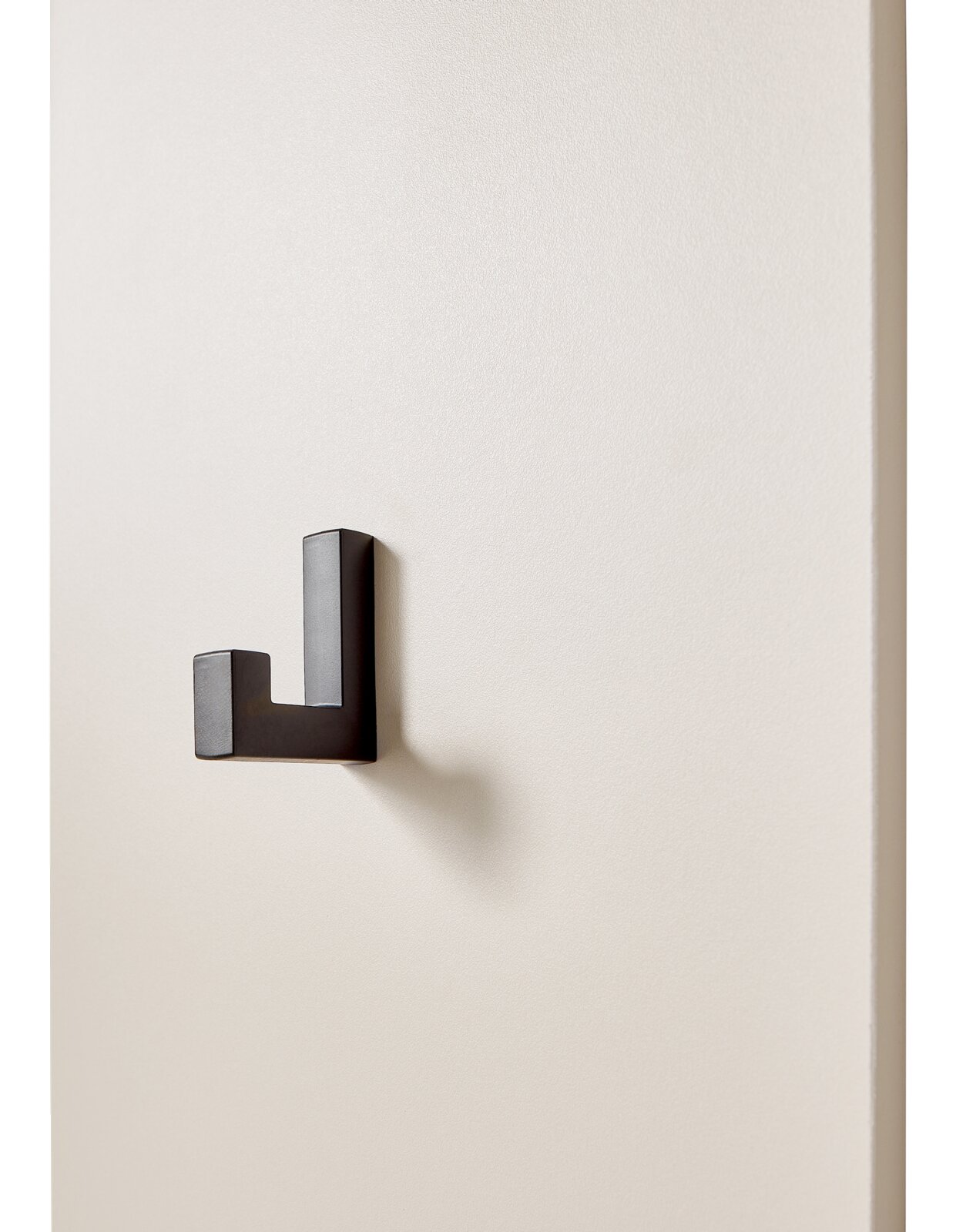 Schwarzer, rechtwinkliger Wandhaken aus Metall an heller Wand, seitliche Perspektive mit sichtbarem Schattenwurf